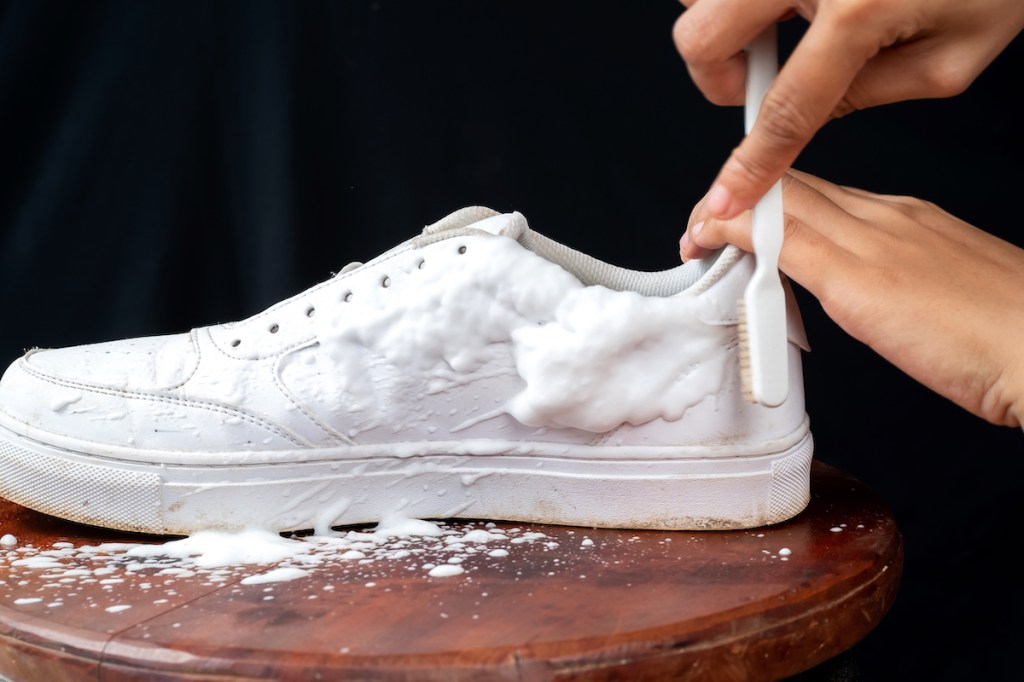 Woman's hands cleaning white sneakers with toothbrush
