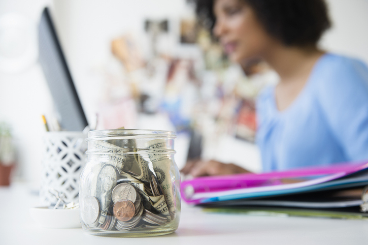 Close up of change jar on desk with a woman on her computer learning how to save money at dollar tree 