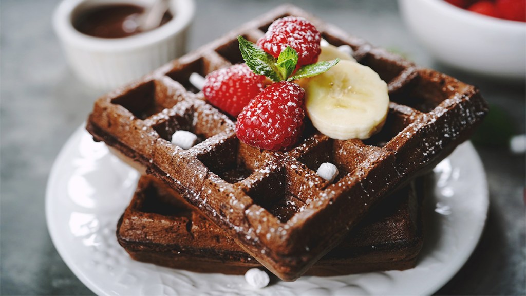 Nutella banana waffles served on a plate with extra sliced bananas and raspberries