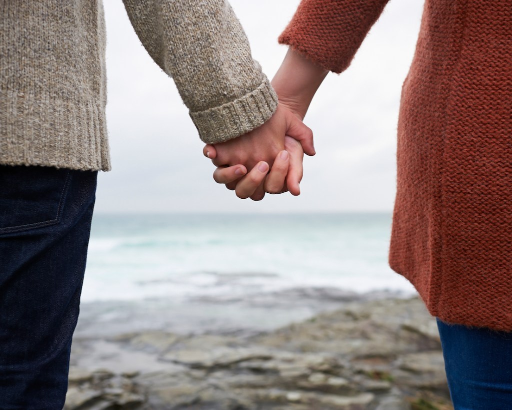Close up of couple holding hands on coastline. ( Scorpio and Virgo Compatibility) 