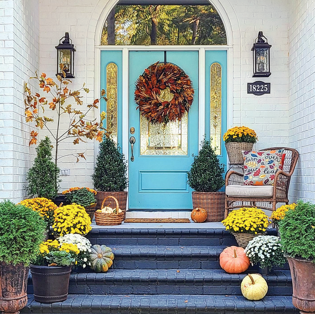 Seasonal fall and Halloween doorway look layered pumpkins and mums up stairway to blue front door