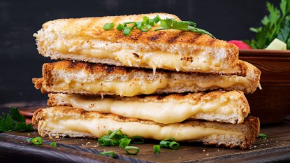 Melty grilled cheese sandwich stacked on a wooden cutting board