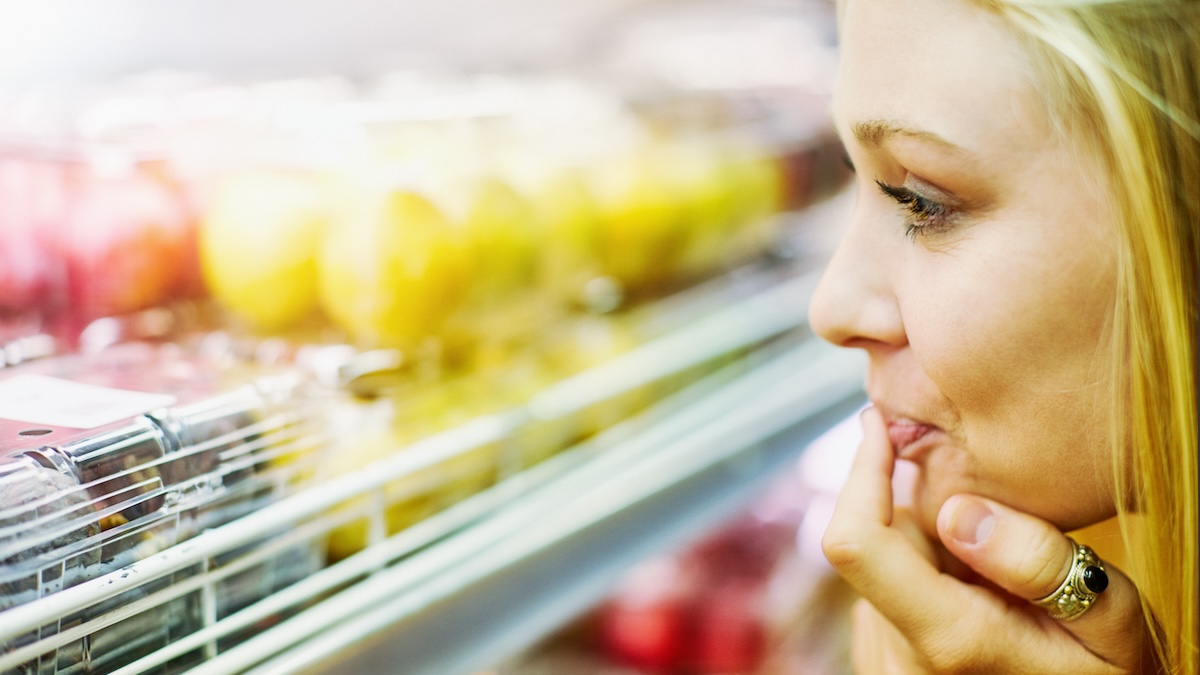 Young woman looks delighted as she examines the fruit on refrigerated shelves in a supermarket.