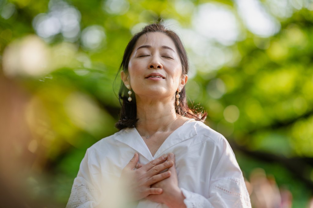 mature woman putting her hands over her heart while practicing heart brain mindfulness outside