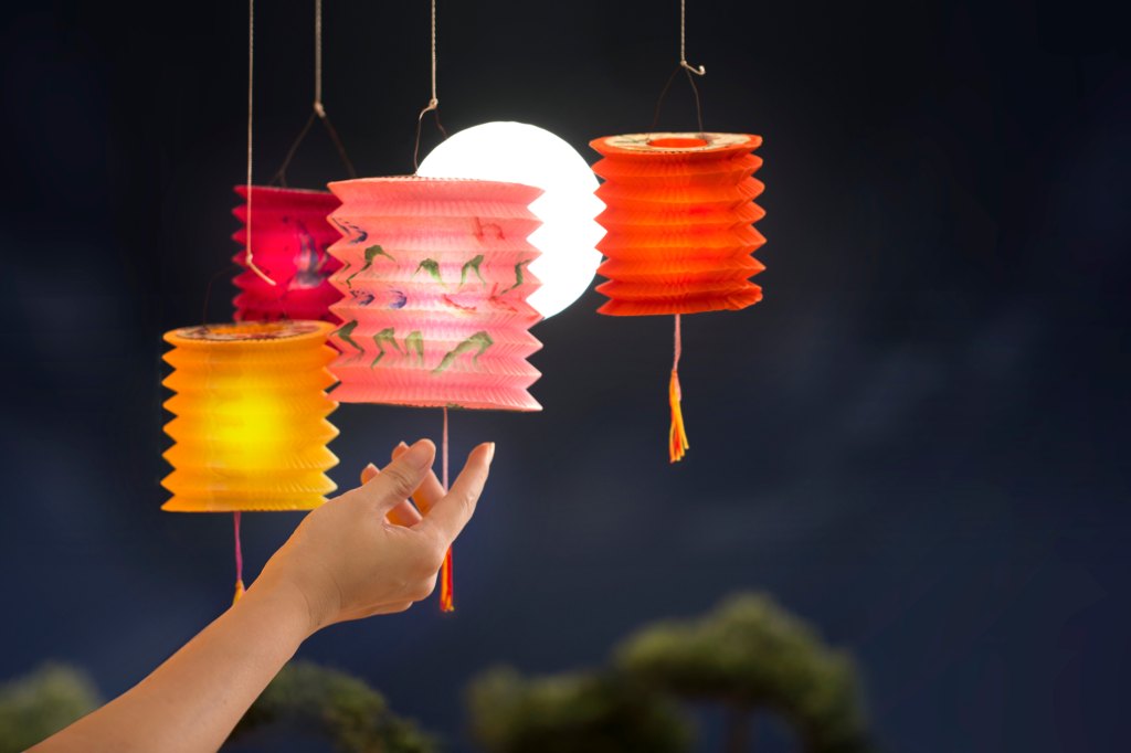 woman's hand holding colorful lanterns on full moon sky during mid-autumn festival