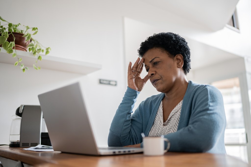 woman sitting at table looking frustrated at her laptop