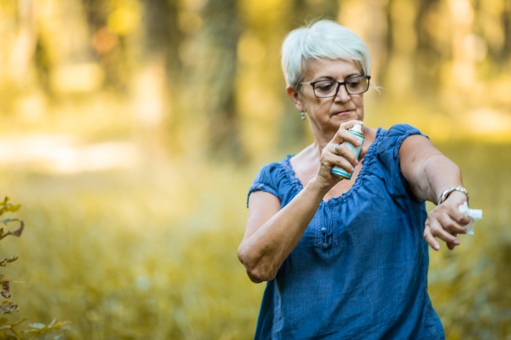 mature woman outside spraying bug spray on arm to prevent west nile virus