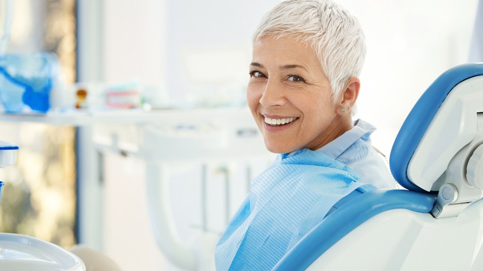 Woman sitting in a chair a the dentist and smiling because her self care approach healed her gum disease