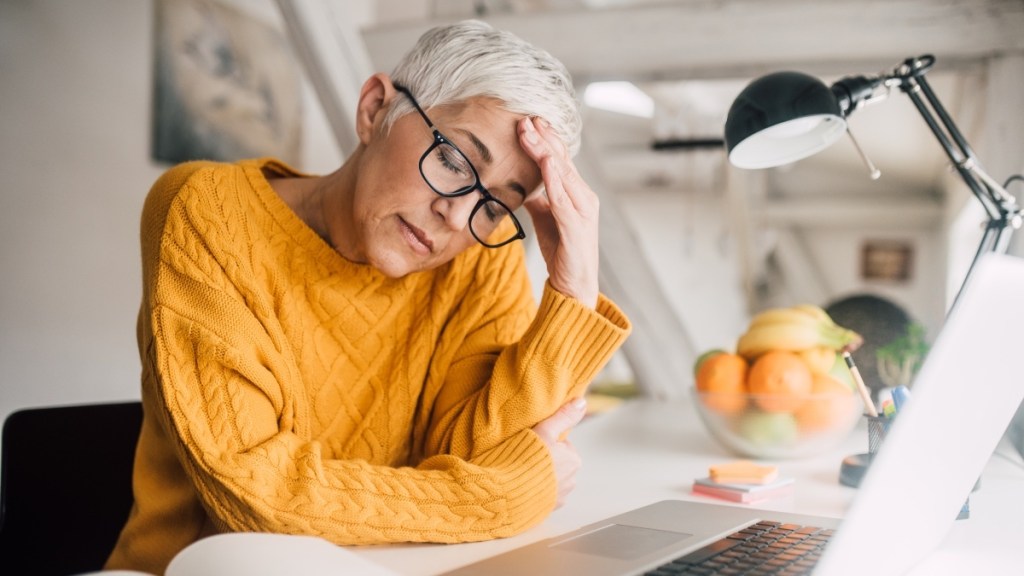 A woman with grey hair, black glasses and a yellow shirt experiencing burnout