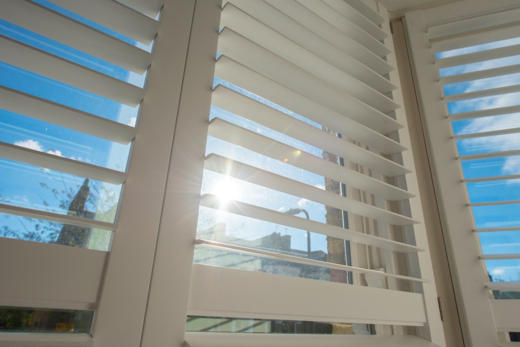 20 Brilliant Uses For Vinegar and Dish Soap: A general interior view of open Plantation Shutters covering a window with bright sunlight flare shining through  within a home