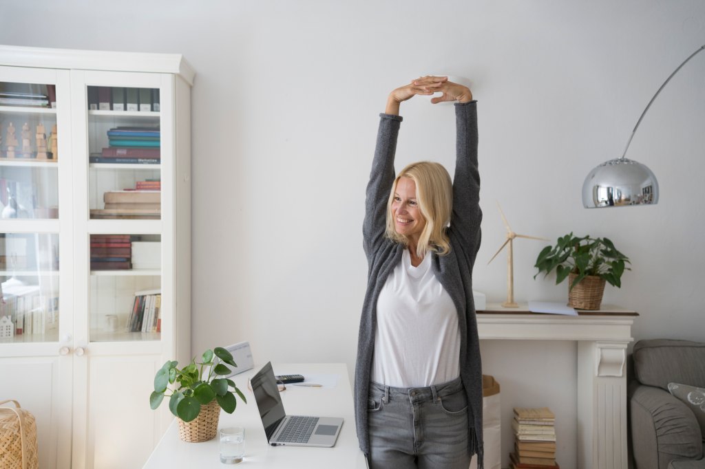 mature woman stretching at her desk for less sitting time to reduce lower back pain