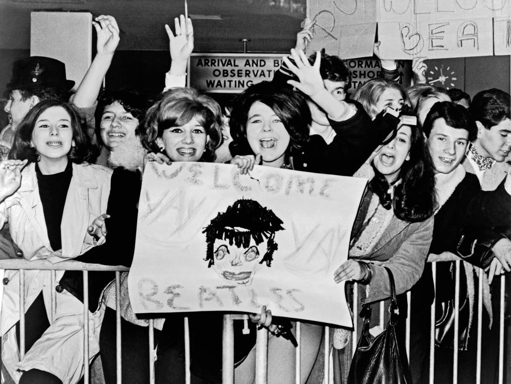 Screaming teenagers wave a crude sign as they welcome 'The Beatles' to John F. Kennedy Airport, New York, New York, February 7, 1964.