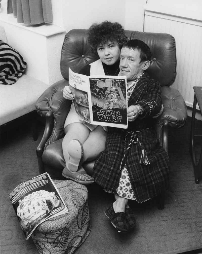 English actor Kenny Baker (1934 - 2016), famed for his role as R2-D2 in the film 'Star Wars', with his wife Eileen at their home in Bushy, London, circa 1977. They are reading an official collector's edition of a 'Star Wars' magazine.