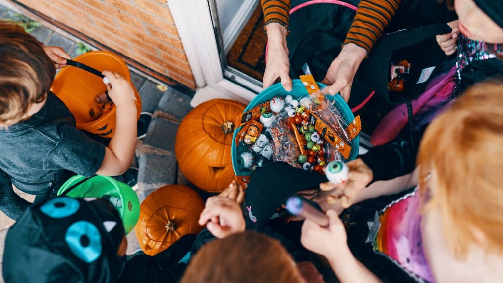 Overhead view of a group of children at a front door taking sweets from a bowl at Halloween. -