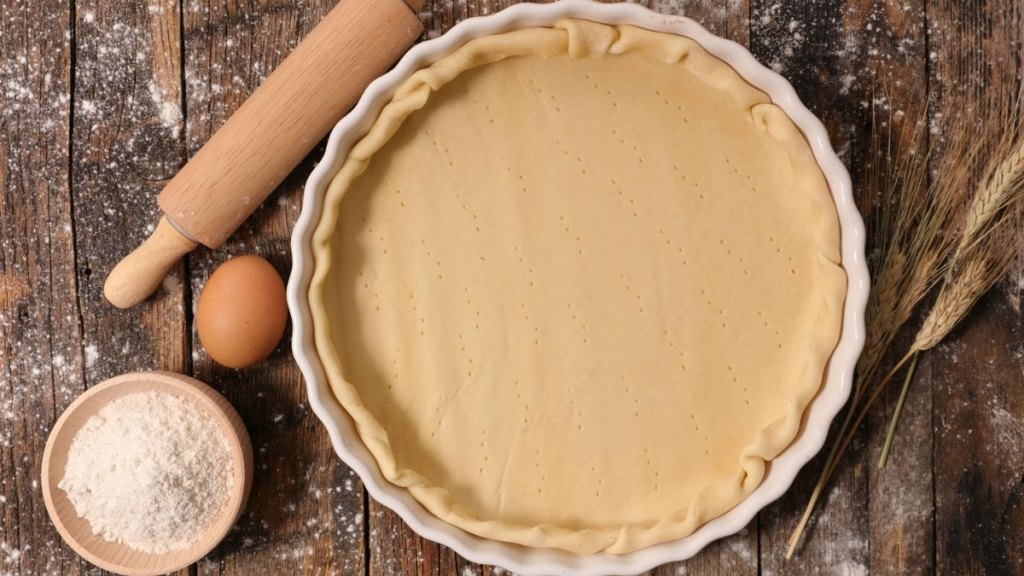 homemade pie crust in dish with rolling pin, flour and eggs