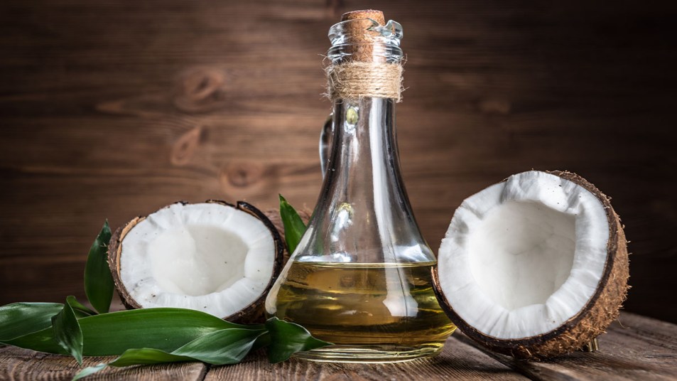 Bottle of coconut oil to use for weight loss on wooden surface with two coconut halves next to it