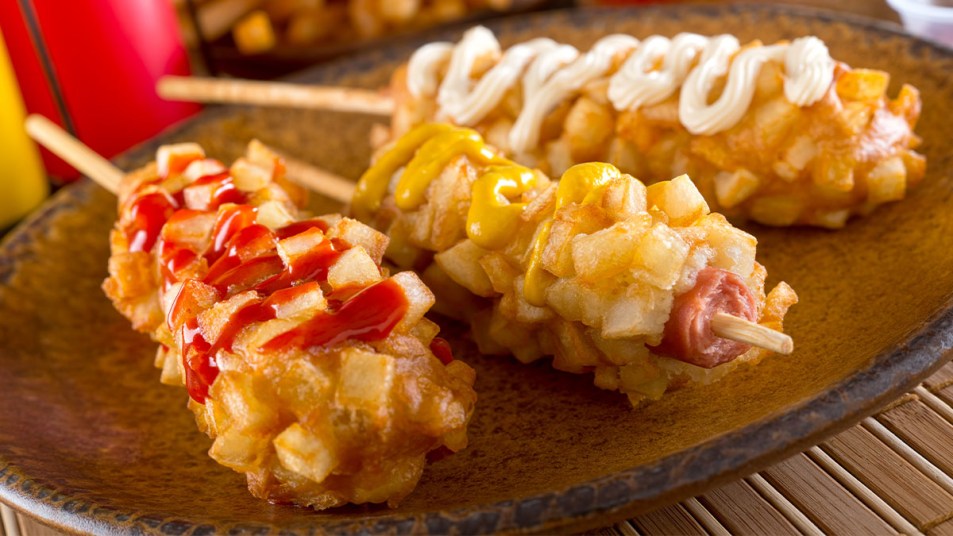 Trio of Korean corn dogs: hot dogs on a stick, dipped in batter, rolled in French fries, then deep fried