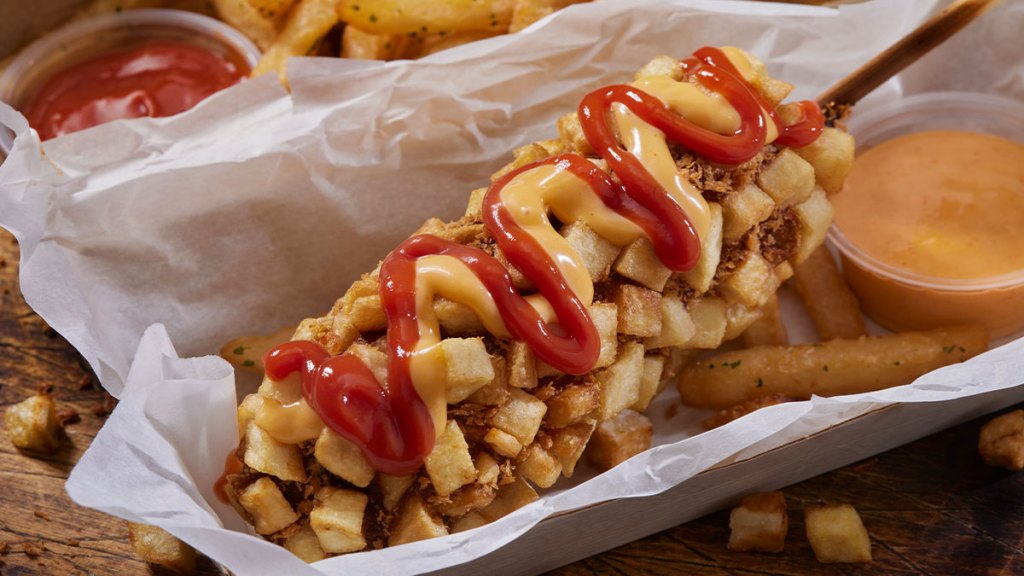 Korean corn dog (hot dogs on a stick, dipped in batter, rolled in French fries, then deep fried) topped with ketchup and mustard