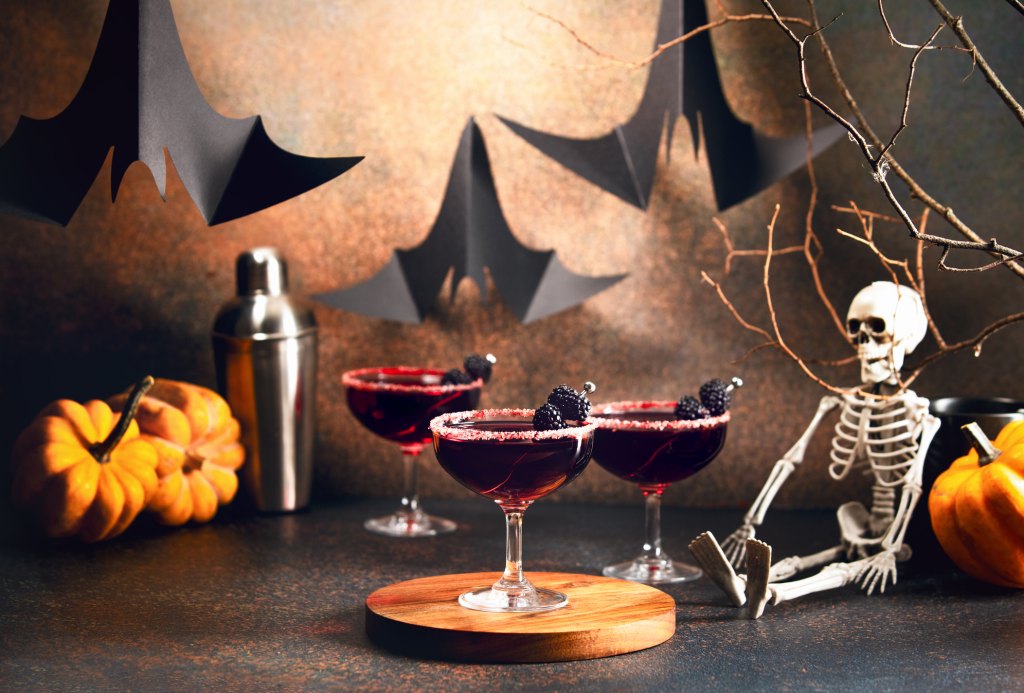 ready-to-drink mocktails decorated with bramble are waiting for the Halloween party guests on a counter decorated with pumpkins and skeleton