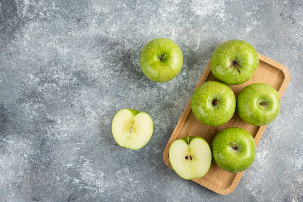 bunch of whole and sliced Granny Smith green apples on cutting board