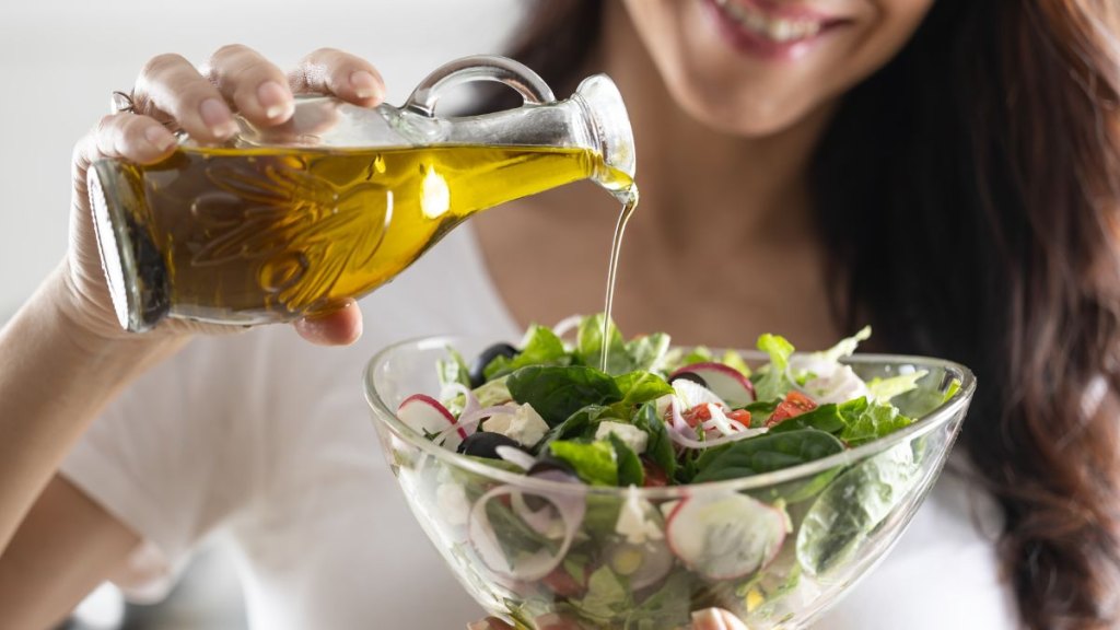 Young woman pouring olive oil in to the salad. Healthy lifestyle eating concept.