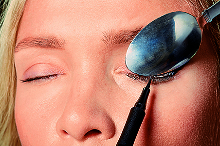 A woman using a spoon to create winged eyeliner