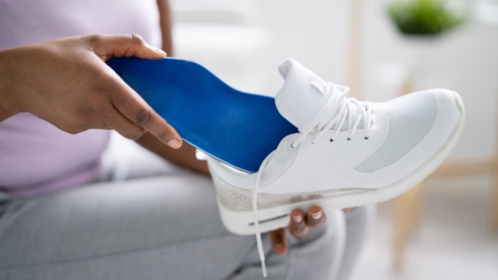 A woman slipping blue insoles into white sneakers for top of foot pain