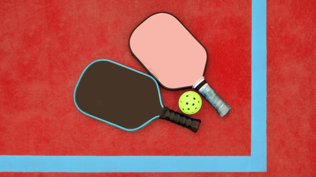 Two pickleball paddles on a red court beside a ball