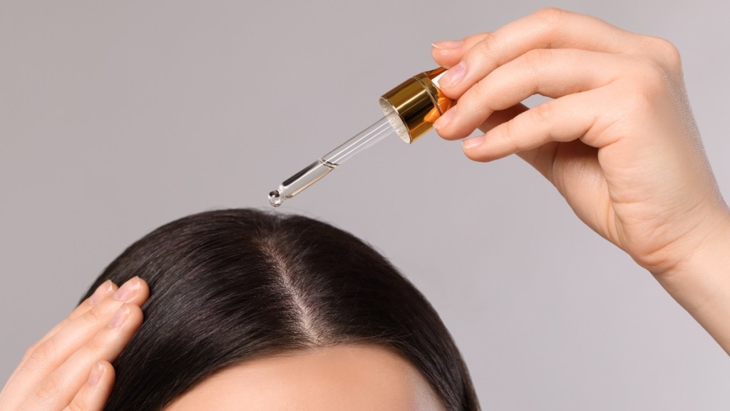 A close up of a woman applying black seed oil to her scalp and hair using a small dropper