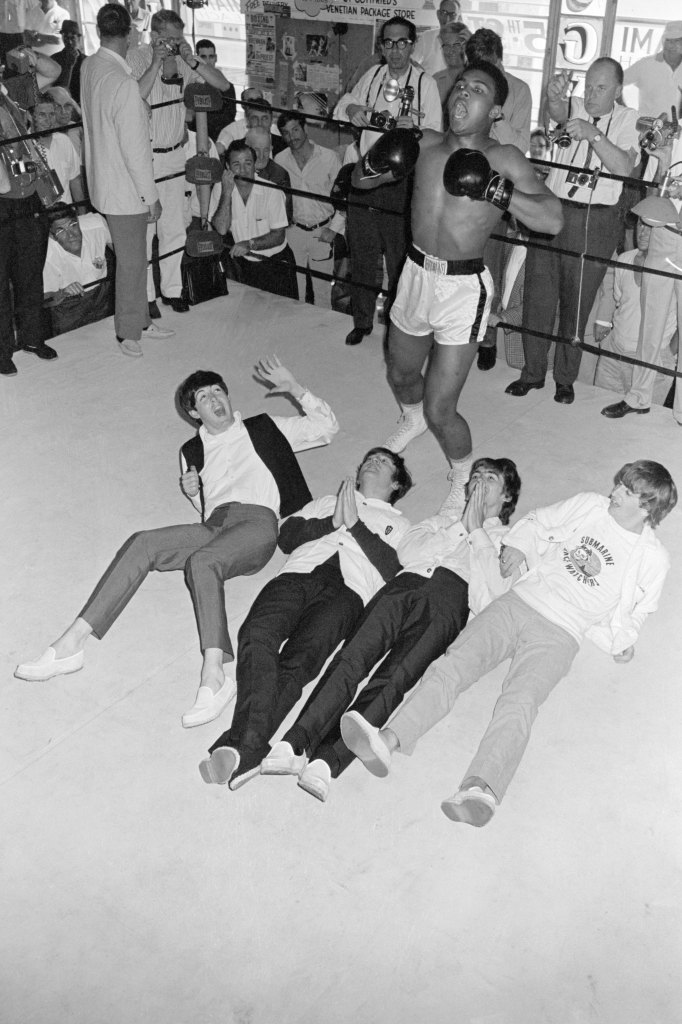 Heavyweight contender Cassius Clay stands above the Fab Four, pounding his chest for photographers at his 5th Street gym. The Beatles, Paul, John, George, and Ringo (l-r) are in Miami for their second appearance on The Ed Sullivan Show. Cassius Clay is currently training for his February 25 heavyweight bout against Sonny Liston.