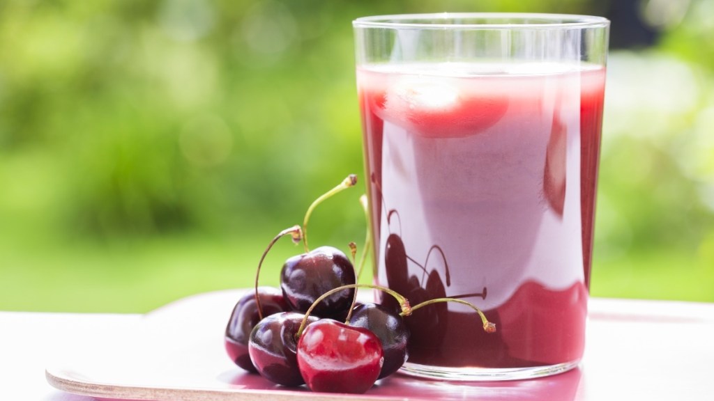 A glass of tart cherry juice beside cherries, which can help block gout attacks