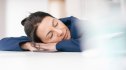 A middle aged woman with her head on the desk sleeping because she's in an afternoon slump