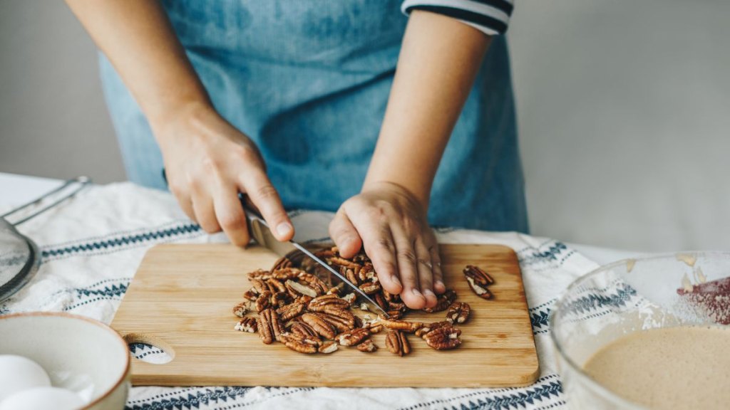 Woman chopping pecan nuts for a cake and using smartphone to read the recipe