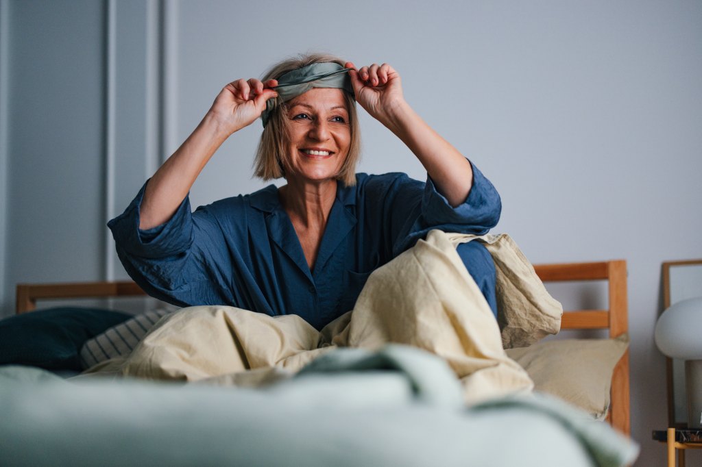 Close up shot of a beautiful cheerful senior woman getting up in the morning and taking off a sleeping mask. She is smiling and looking away.