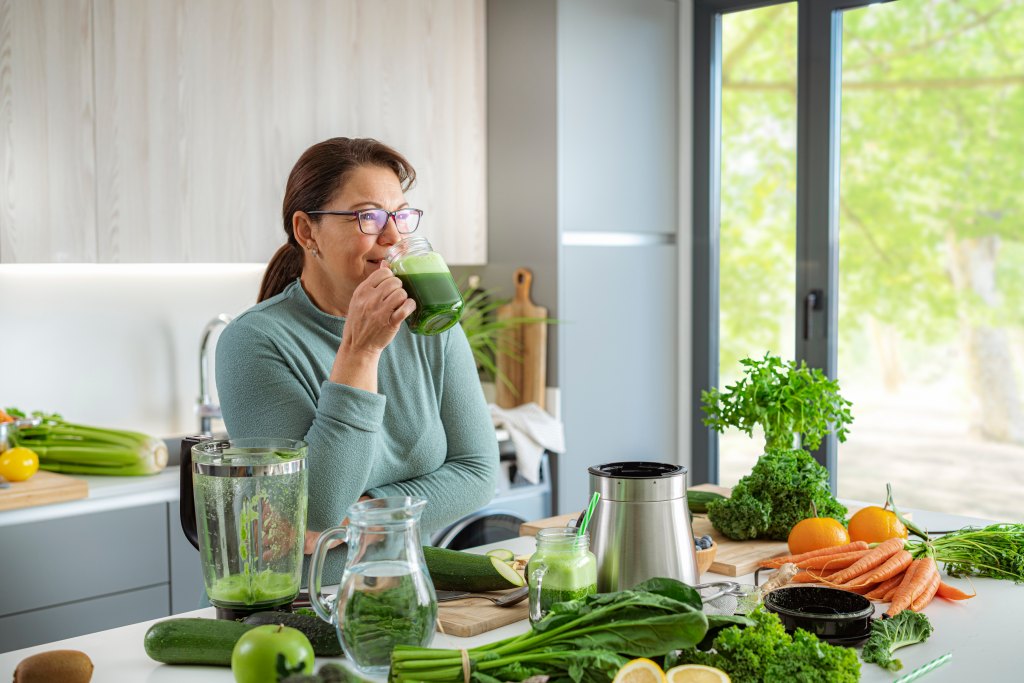 woman in kitchen drinking green juice