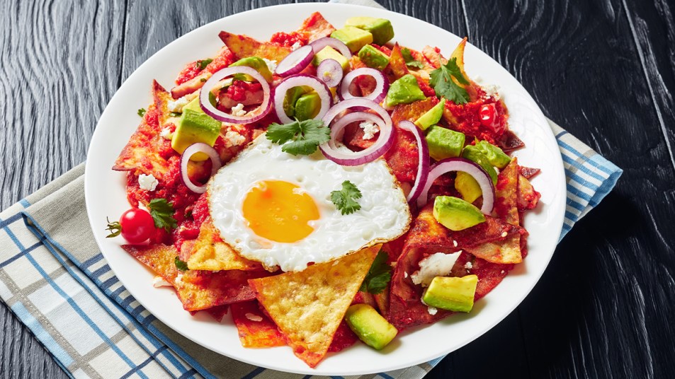 Plate of breakfast nachos with chips topped with salsa, fried egg, onions and avocado