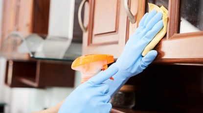 rubber gloved hand cleaning a kitchen cabinet