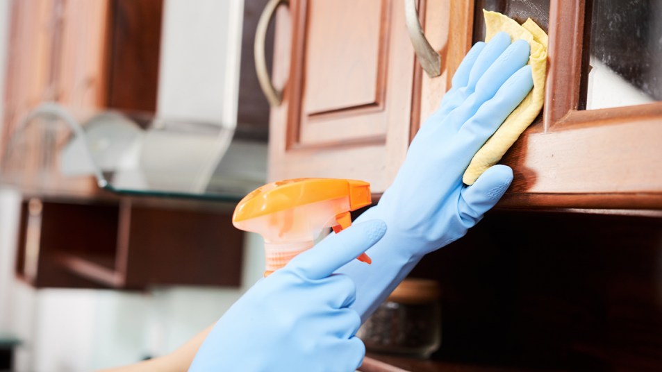 rubber gloved hand cleaning a kitchen cabinet