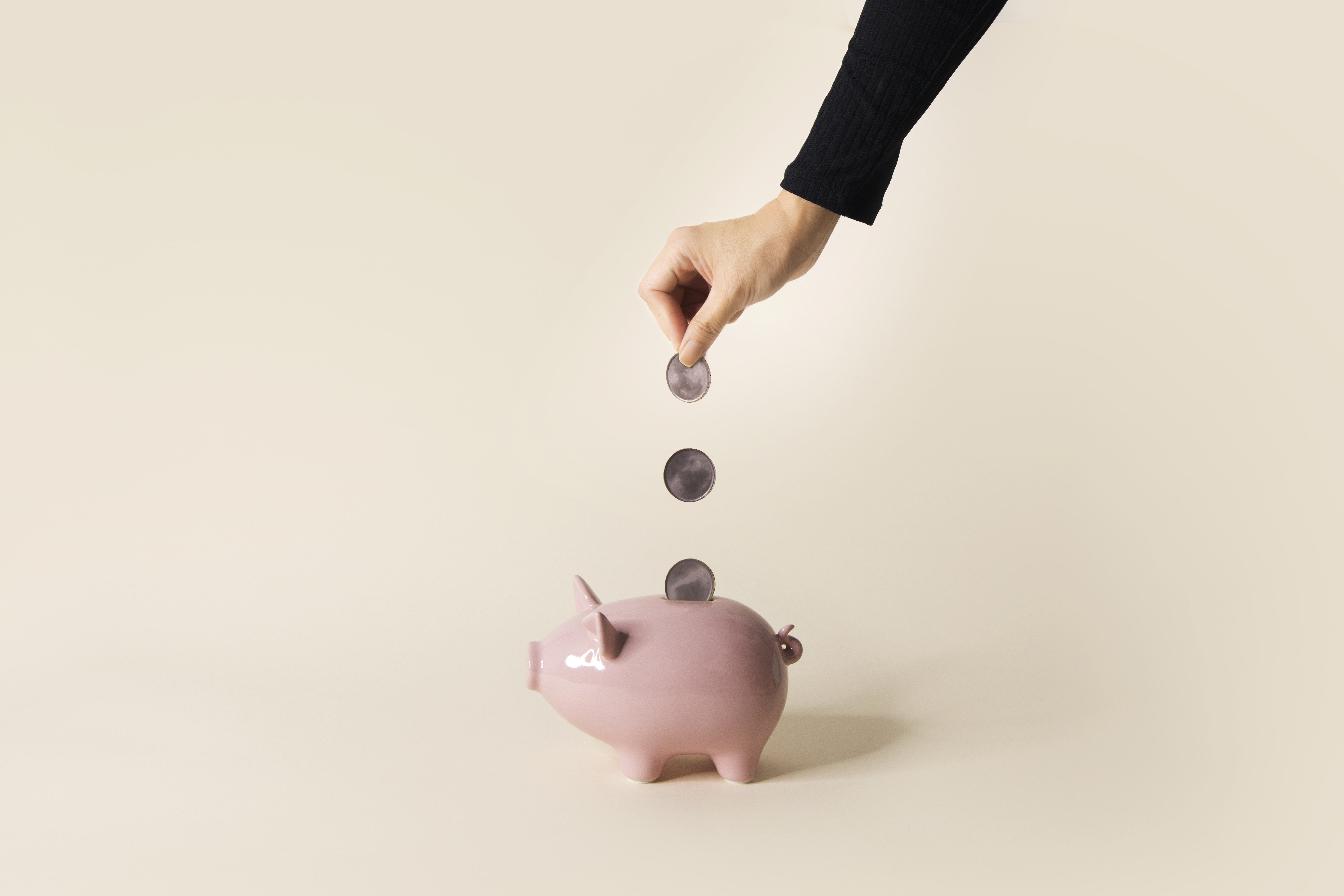 Hand dropping coins into one piggy bank.