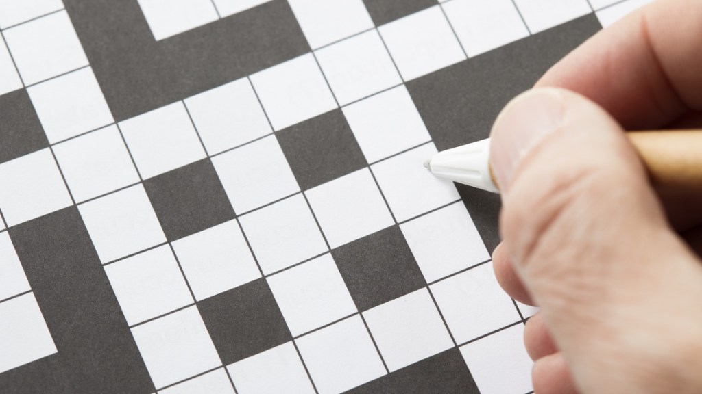A crossword puzzle with a hand holding a pen