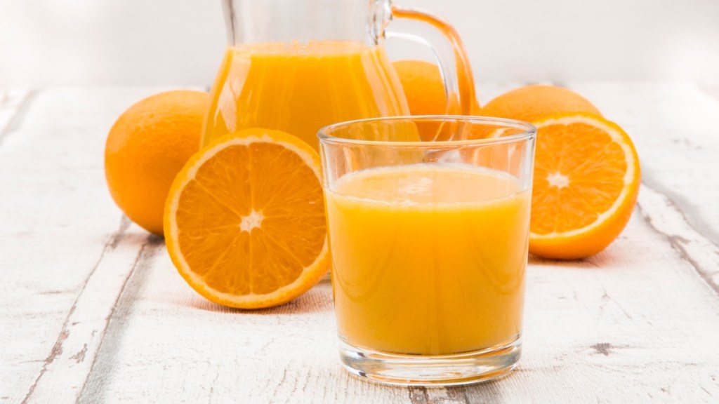 A glass of orange juice beside a pitcher of orange juice and freshly-sliced oranges