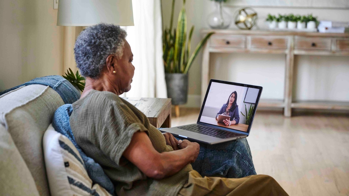 an older woman conducts a telehealth virtual consultation with her doctor on her sofa