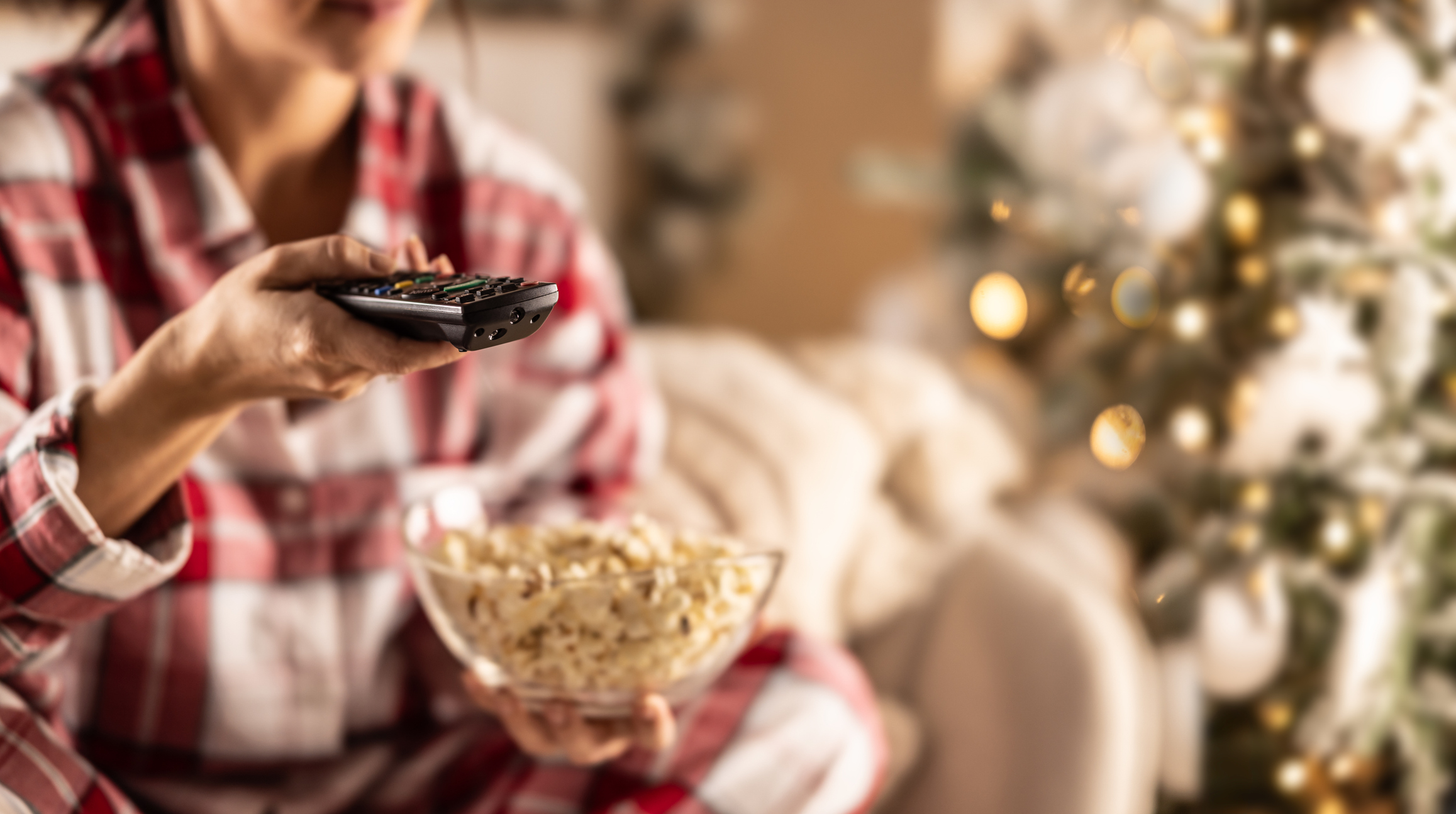 woman in pajamas holding a tv remote with popcorn to watch iconic holiday movies