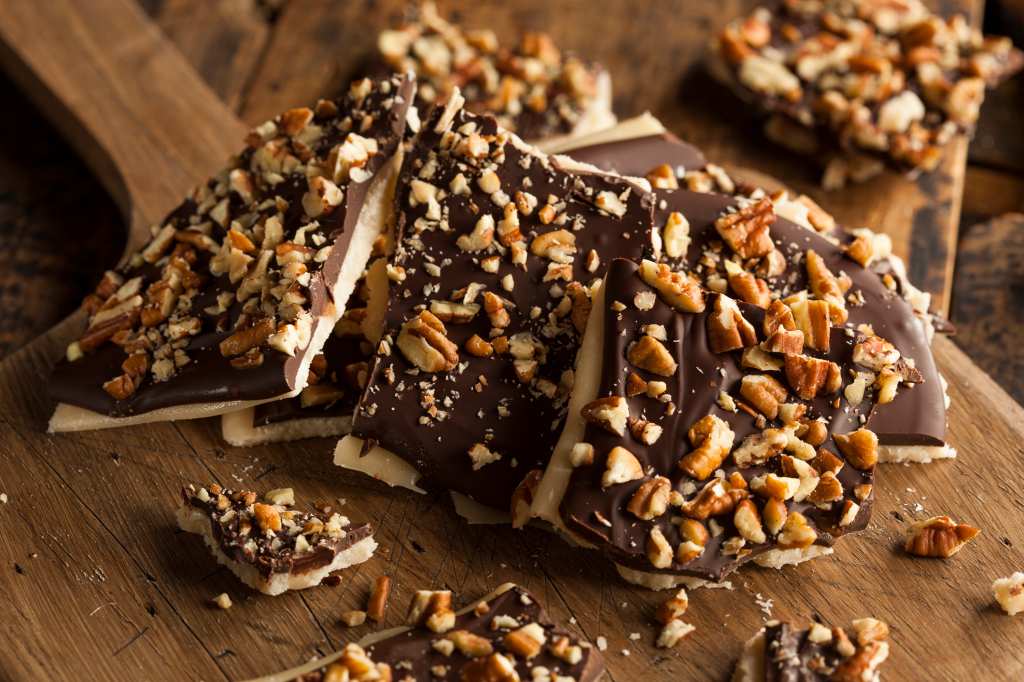 homemade 'Christmas Crack' with nuts broken into pieces on wooden cutting board