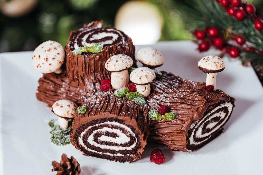 holiday yule log cake on white plate in front of Christmas tree