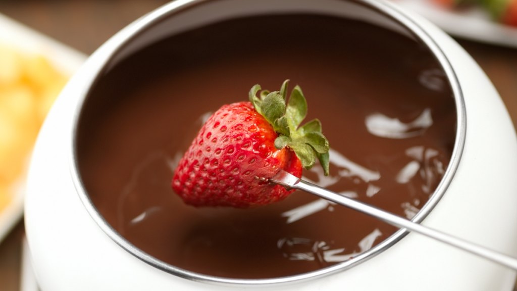 A strawberry being dipped in chocolate fondue