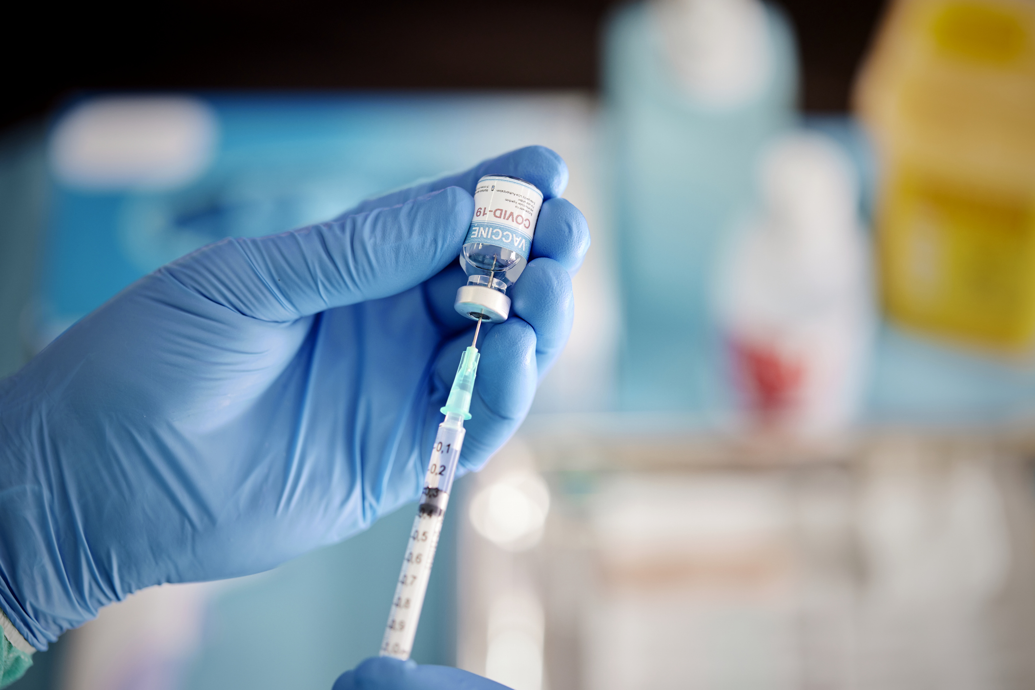 A healthcare Worker hands in surgical gloves pulling vaccine liquid from vial to vaccinate a patient