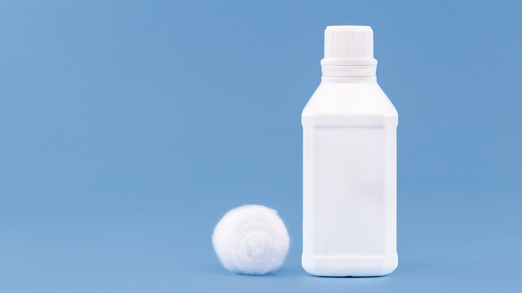 A white bottle of hydrogen peroxide next to a white cotton ball on a blue background