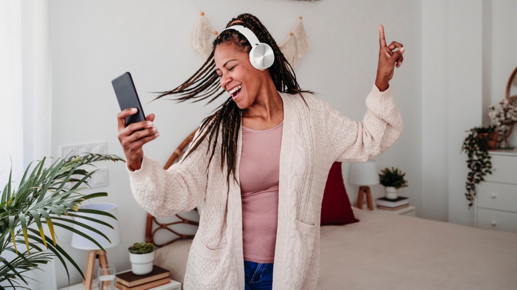 A woman wearing headphones and holding her cell phone while dancing at home to prevent cataracts and glaucoma