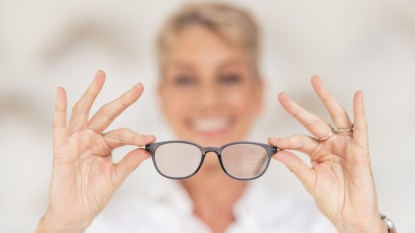 A woman holding a pair of glasses between her two hands wondering if she has glaucoma vs cataracts